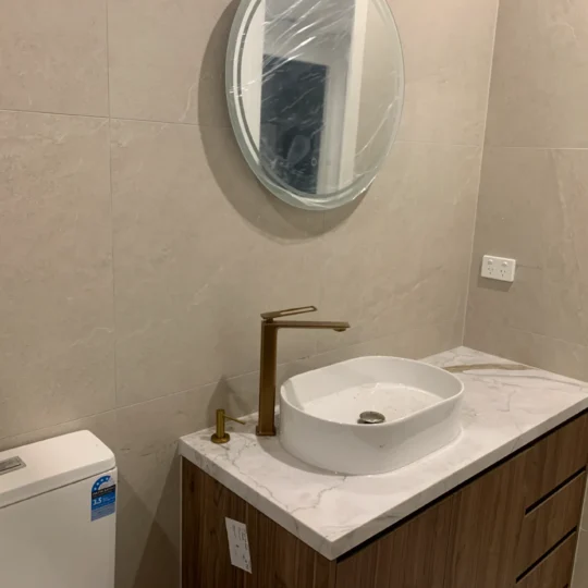 Bathroom renovation with white tiles, marble benchtop, and brass fixtures.