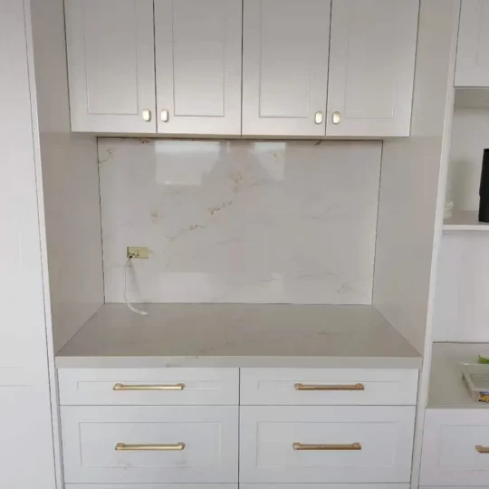 Kitchen renovation with white cabinetry and marble-effect wall tiles.