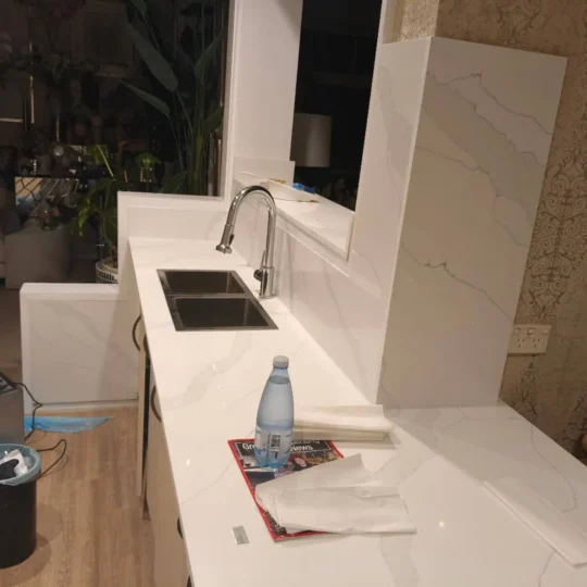 Modern kitchen featuring white engineered stone benchtop and tiles.