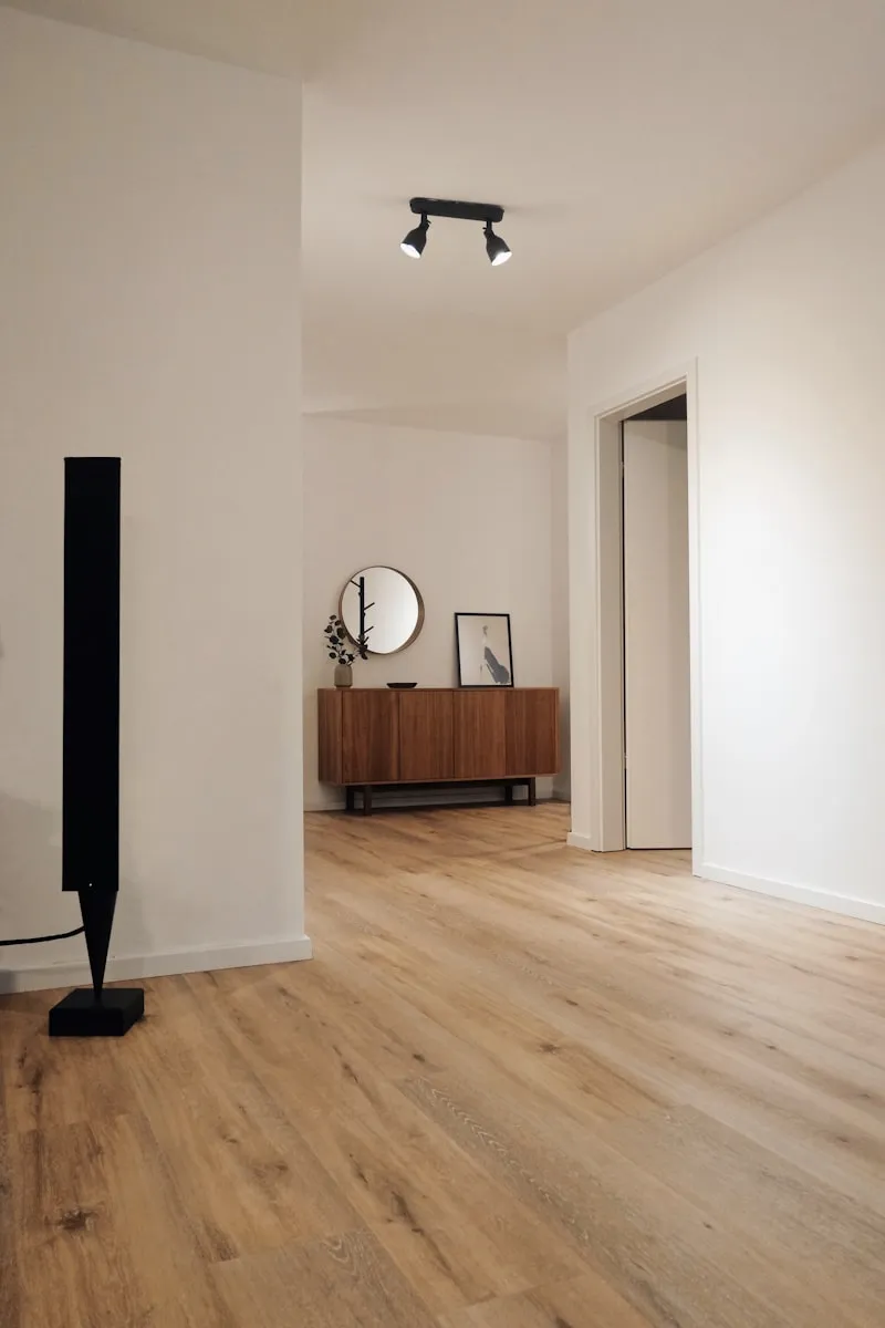 Minimalist interior hallway with wooden flooring, wall mirror, and a sideboard
